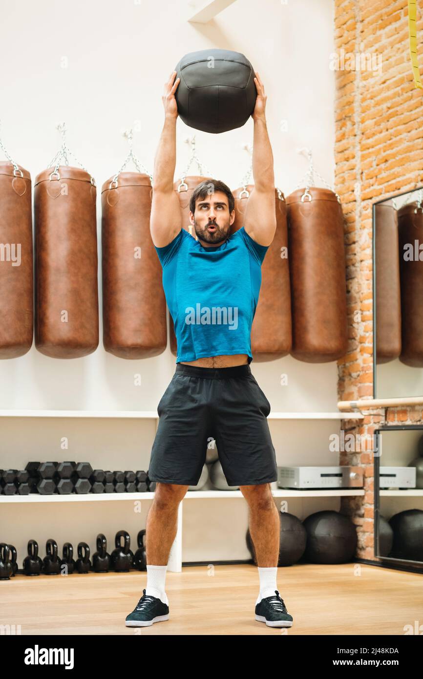 Fit muscular man working out with a Pilates Medicine Ball raising it above his head. Often used for neuromuscular rehabilitation Stock Photo