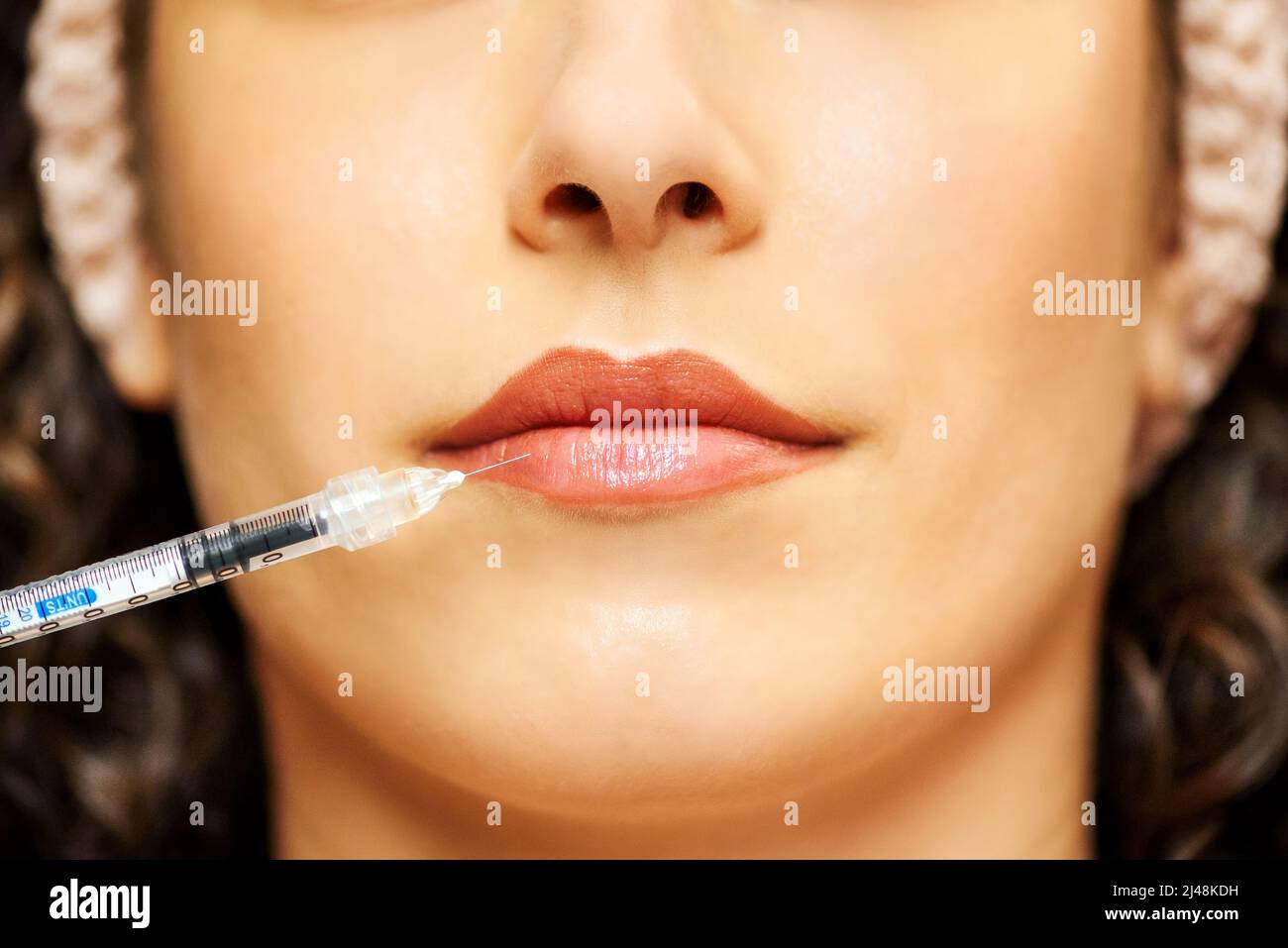Closeup selective focus of syringe with thin needle injecting filler into red lips of anonymous female Stock Photo