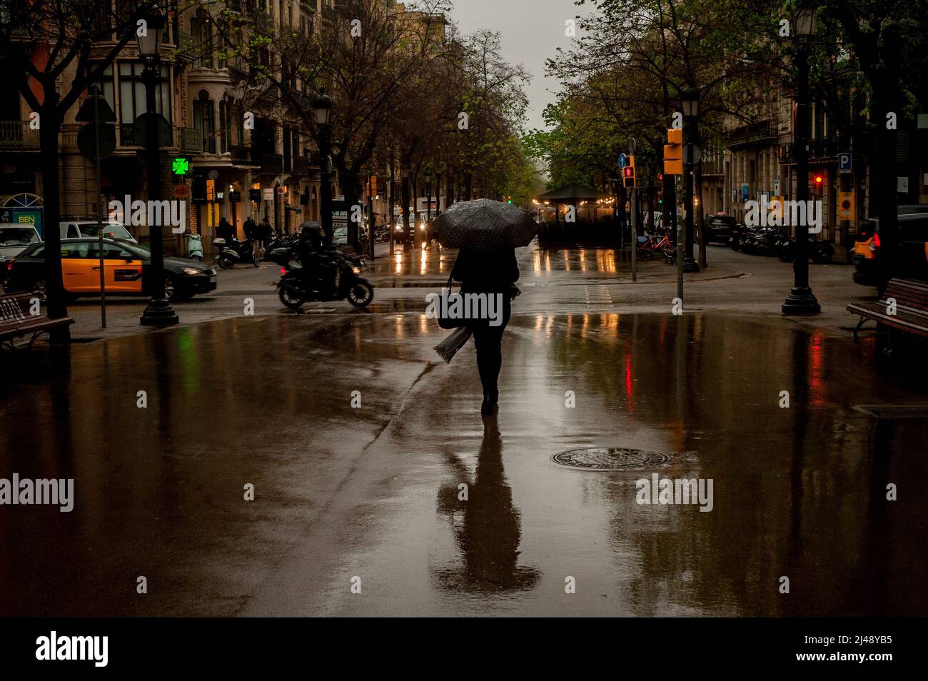 Barcelona, Spain. April 13, 2022, Barcelona, Spain: An early morning commuter walks under the rain along La Rambla de Catalunya St. in Barcelona. Credit: Jordi Boixareu/Alamy Live News Stock Photo