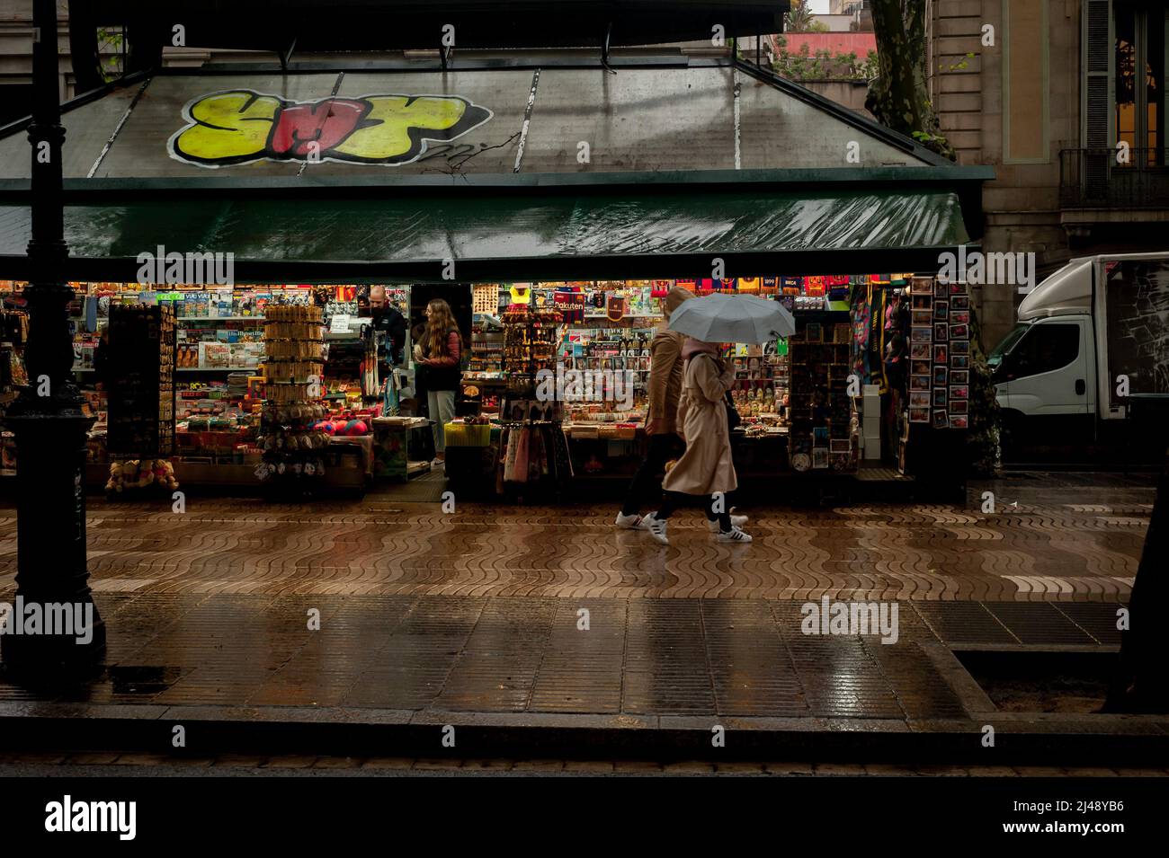 Barcelona, Spain. April 13, 2022, Barcelona, Spain: Early commuters walk past a kiosk in Las Ramblas of Barcelona on a rainy morning. Credit: Jordi Boixareu/Alamy Live News Stock Photo