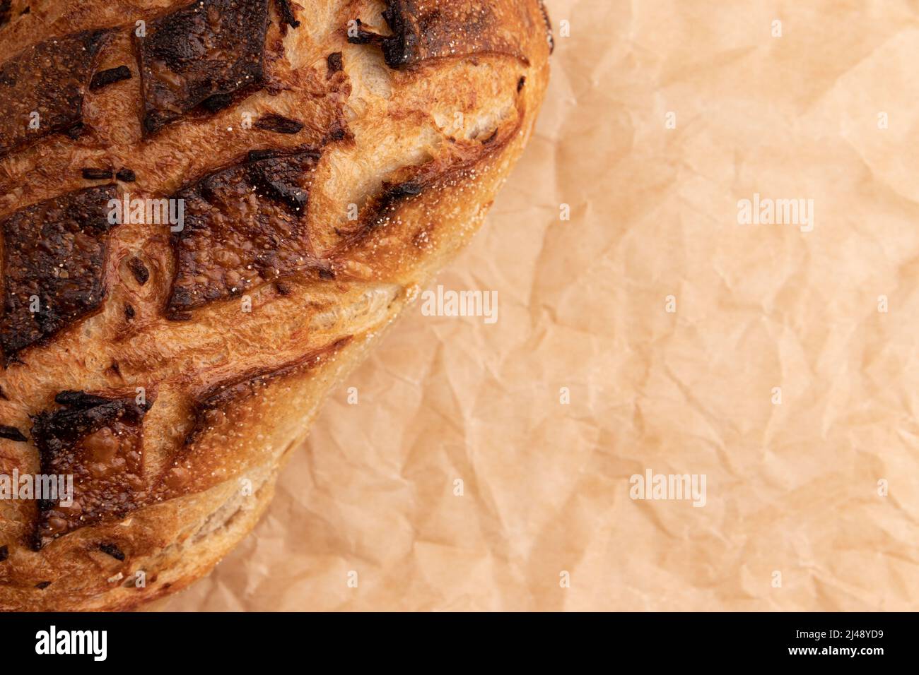 top view of fresh homemade bread with golden crispy crust on parchment for baking, organic loaf with onion close-up and space for text Stock Photo
