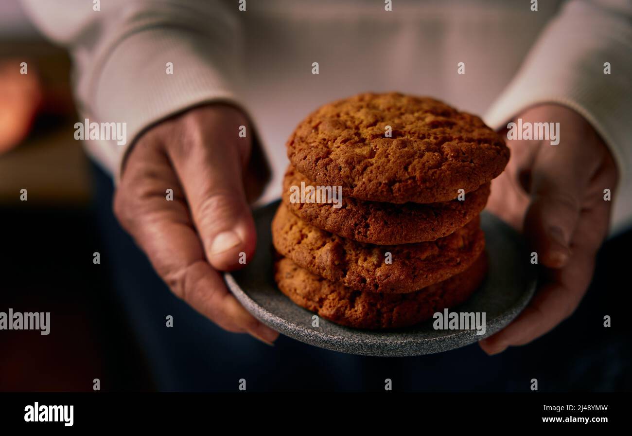 A woman is holding several cookies and a gray ceramic plate in her hands Stock Photo