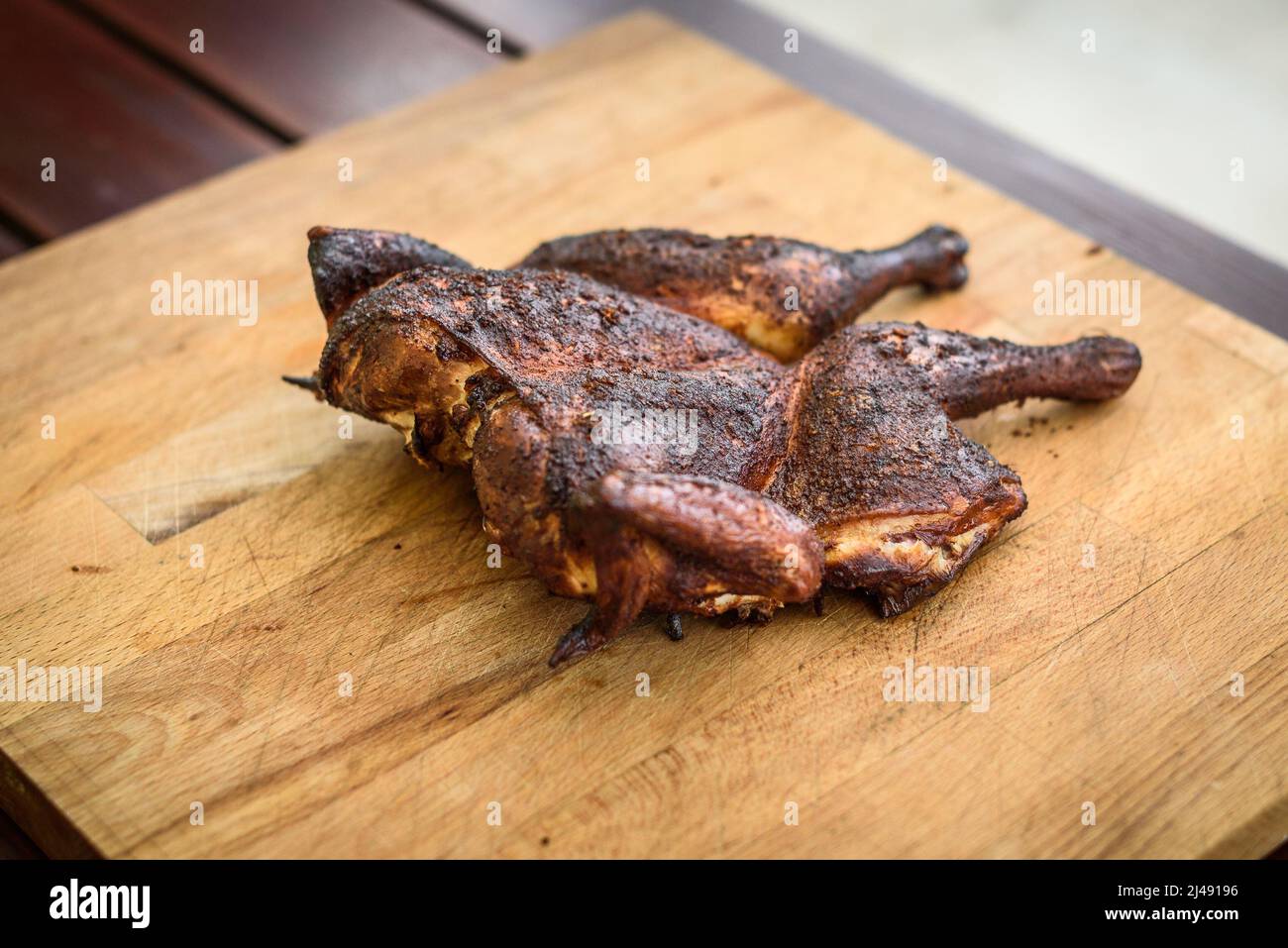 Traditional spatchcocked barbecue chicken al mattone on charcoal grill. Grilling and smoking spatchcock chicken on firewood BBQ grill in nature on fam Stock Photo