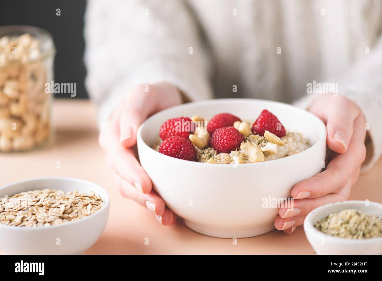 Oatmeal bowl with raspberry, cashew nuts and hemp seeds in female's hands. Clean eating, dieting concept Stock Photo