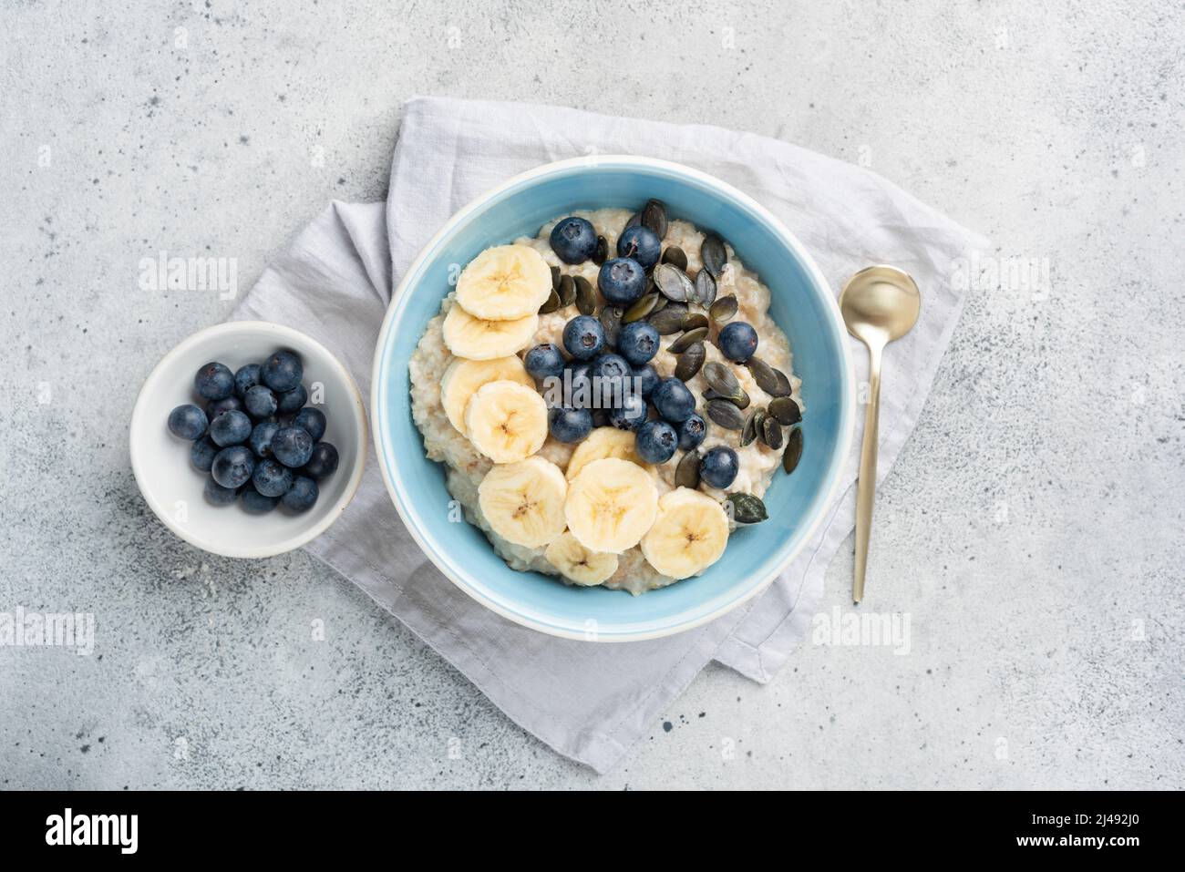 Healthy breakfast oatmeal porridge bowl with fruits and pumpkin seeds on grey concrete background. Top view Stock Photo