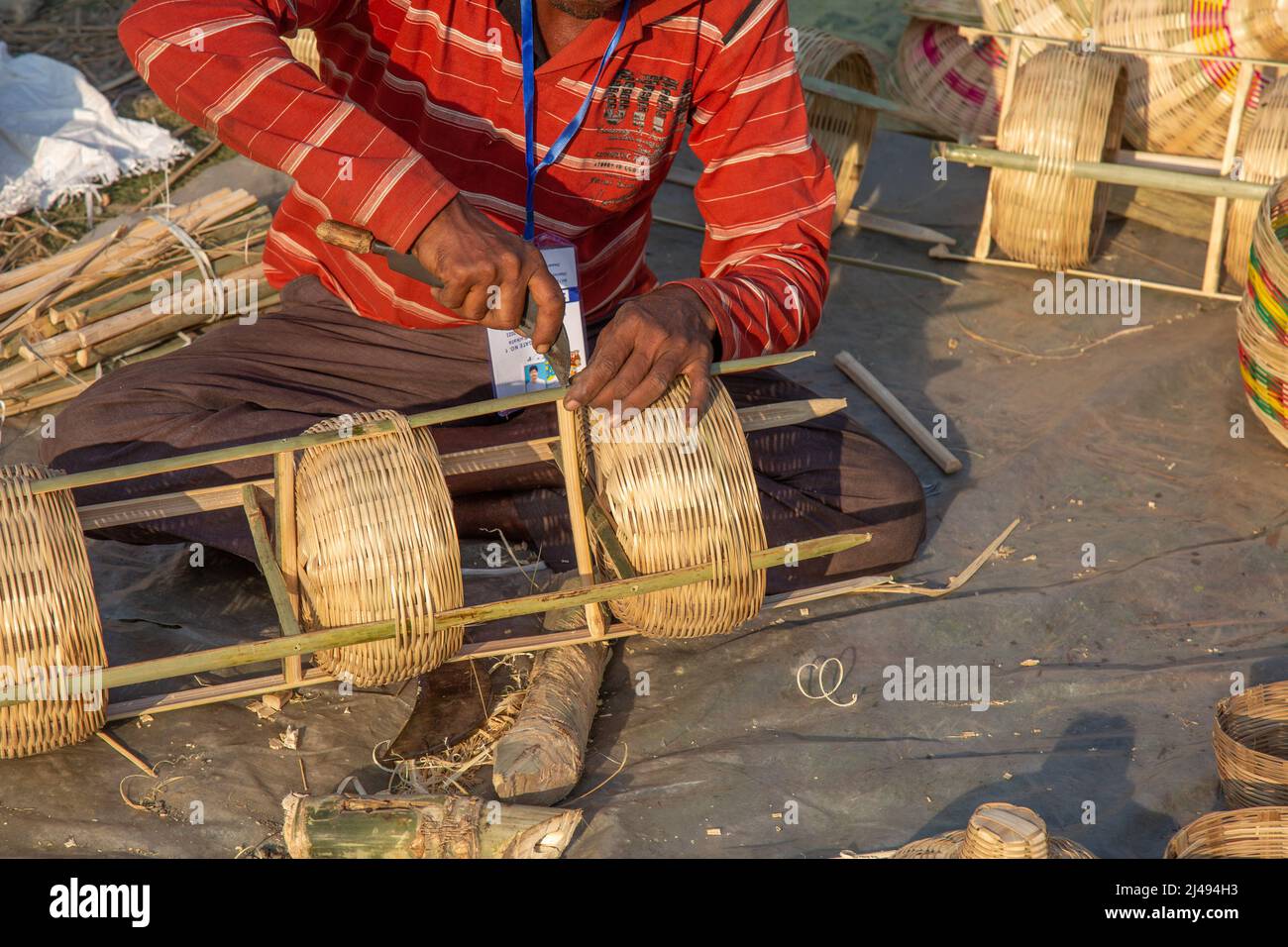 Rural Indian craftsman cutting bamboo sticks with sickle for creating