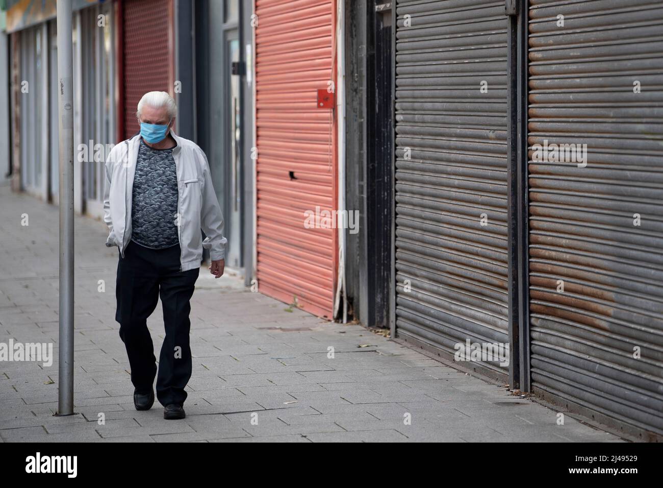 A man wearing a face mask walks past a closed small business during the coronavirus lockdown period in Barry, Wales, United Kingdom. Stock Photo