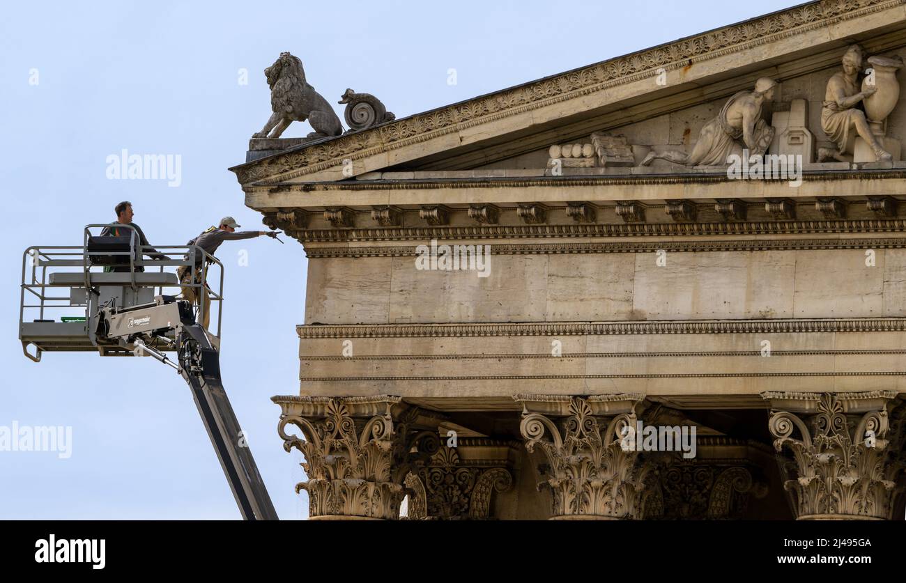 Munich, Germany. 13th Apr, 2022. Two men work on and examine the stone roof façade and frescoes above the entrance to the State Collection of Classical Antiquities on Königsplatz. Greek, Roman and Etruscan masterpieces are on display in the Antiquities Collections. Works of art and utilitarian objects of the Greeks, Etruscans and Romans made of a wide variety of materials such as ceramics, metal and stone are housed in the building. Credit: Peter Kneffel/dpa/Alamy Live News Stock Photo
