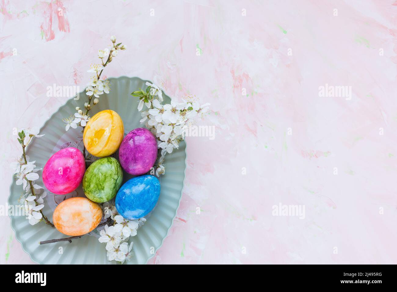 Colorful Easter eggs on plate and spring white cherry blossom flowers on pink background. Easter celebration concept. Top view, flat lay, copy space Stock Photo