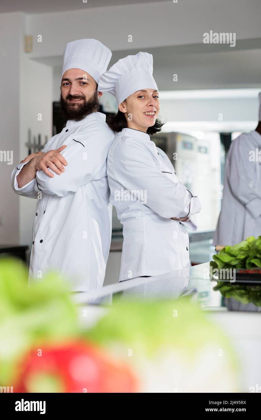 Skilled cooks wearing cooking uniforms while posing back to back in