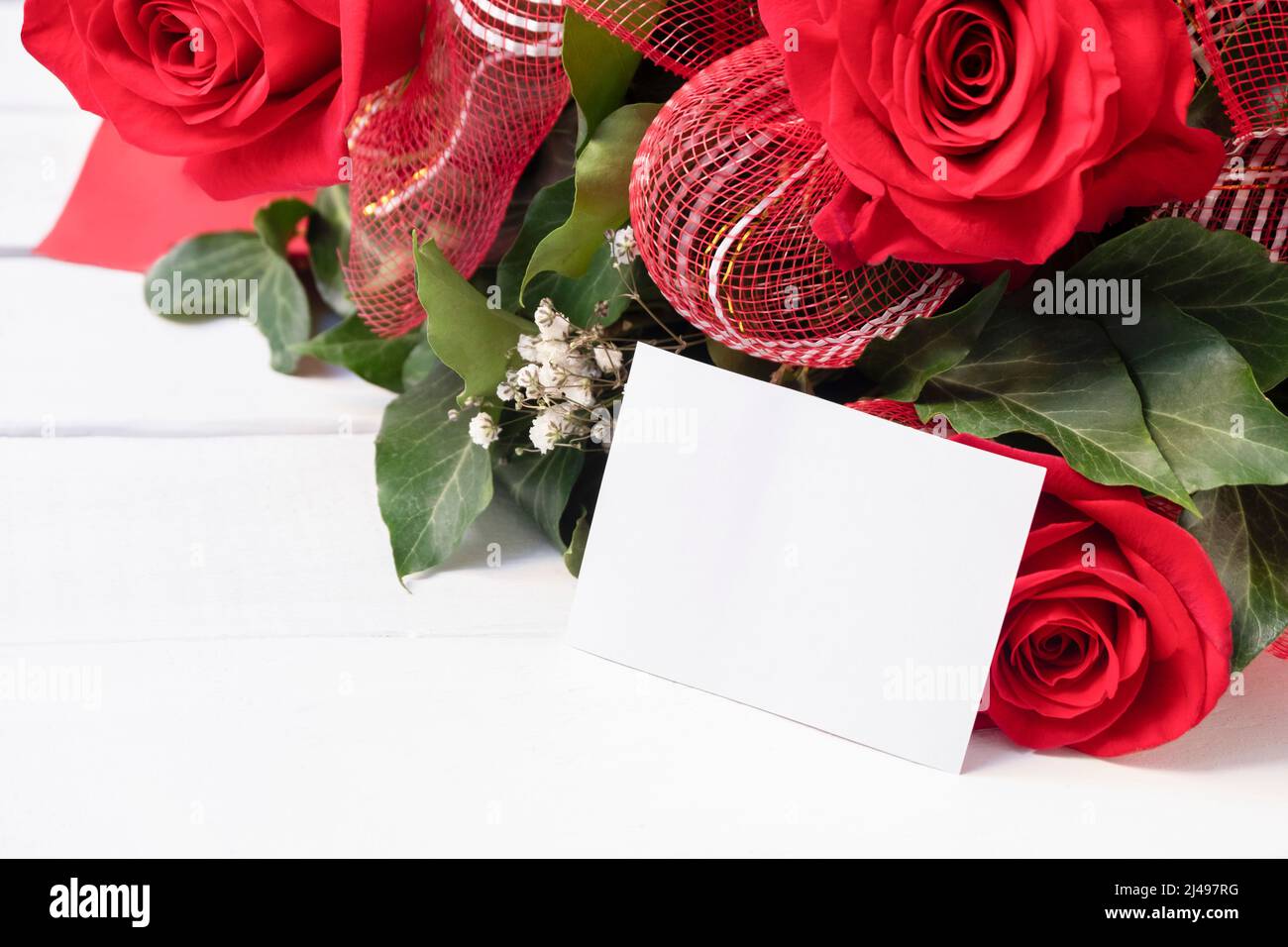 Fresh bouquet of fresh red roses with empty white card on white wooden background. Festive card concept, place for text Stock Photo