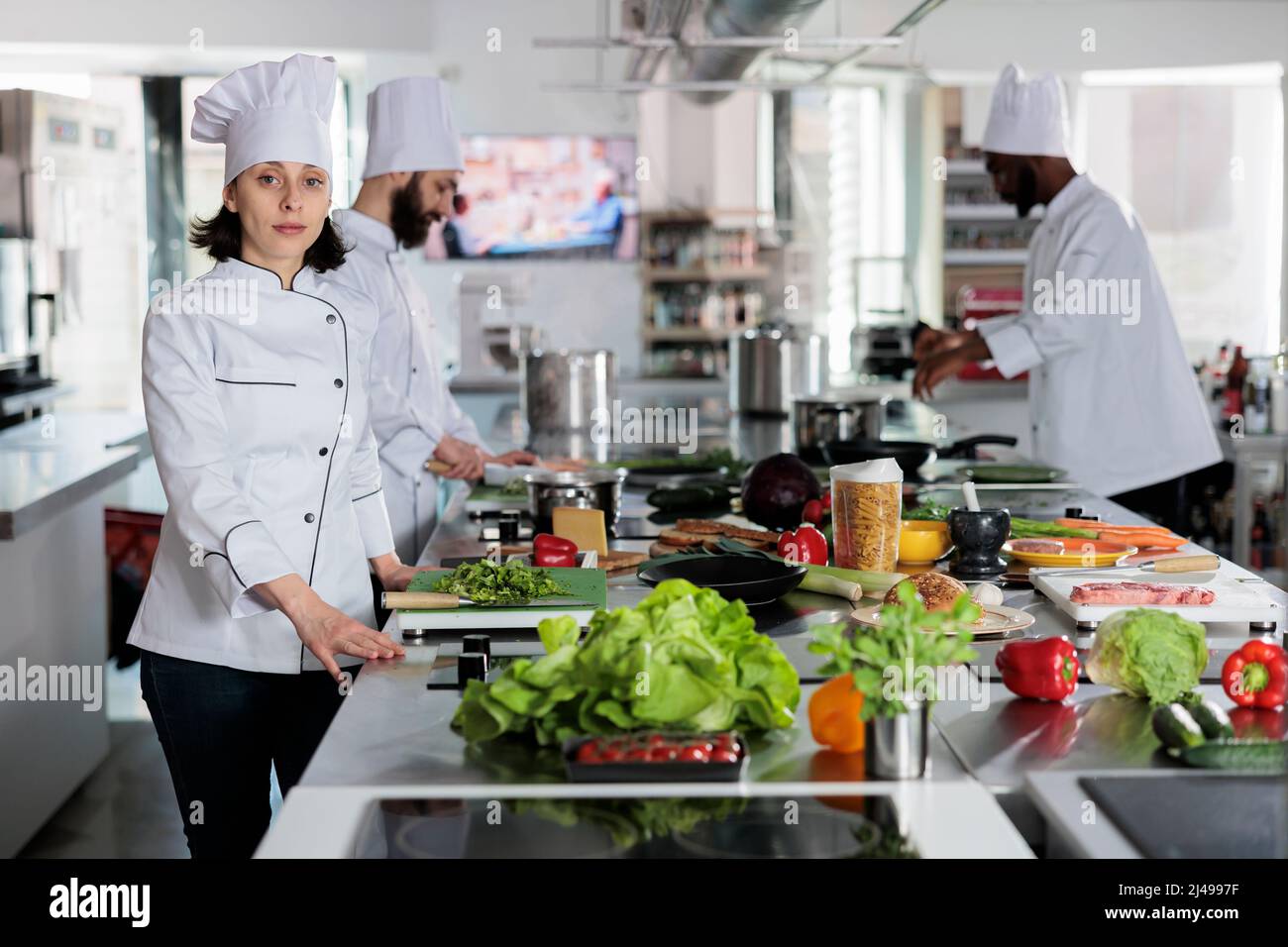 Head cook preparing spices and ingredients for dinner dish while looking confident at camera. Sous chef standing in restaurant professional kitchen space with arms crossed. Stock Photo