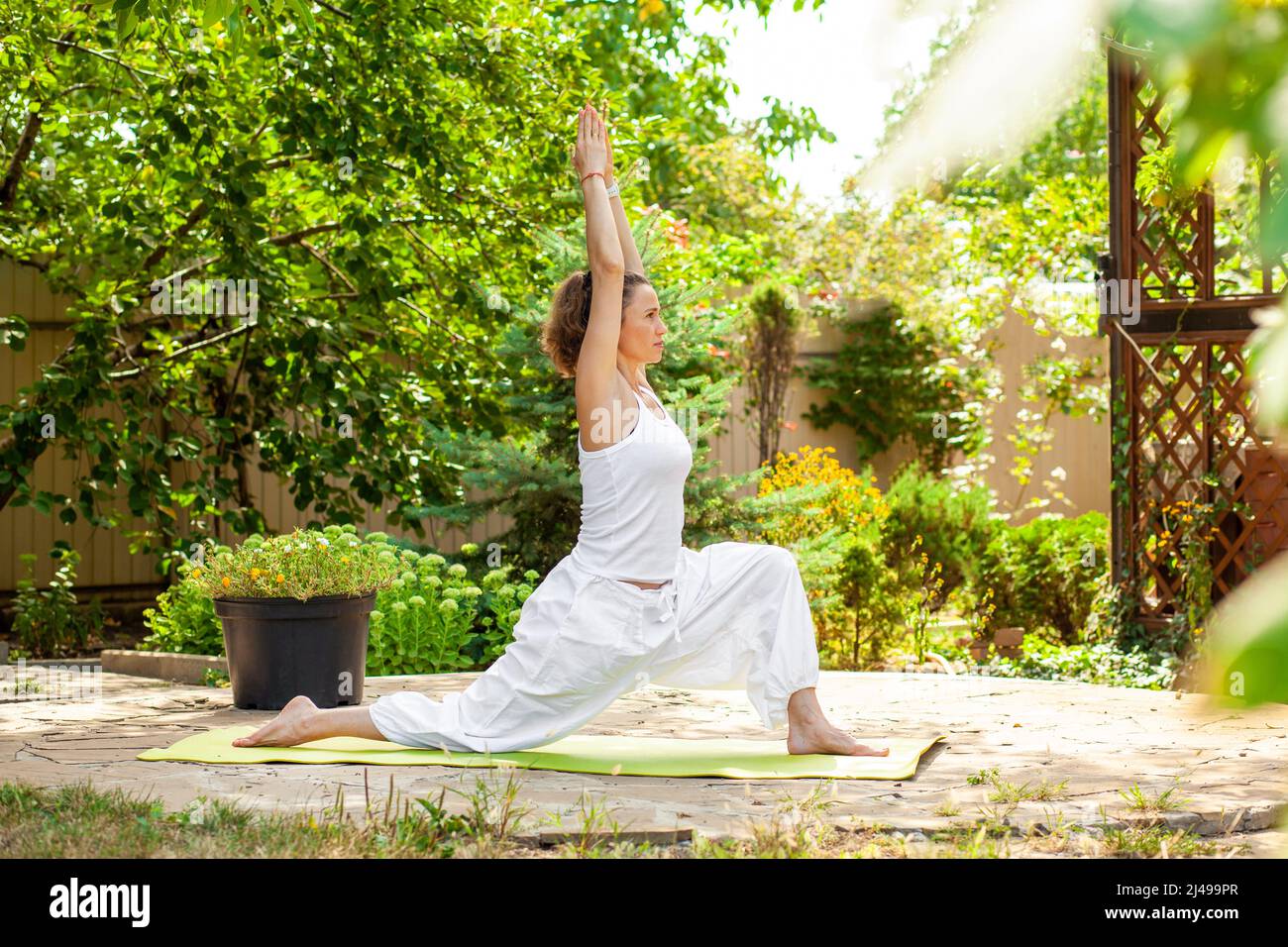 Young woman practices yoga in the summer garden - Warrior Pose, Virabhadrasana I. Stock Photo