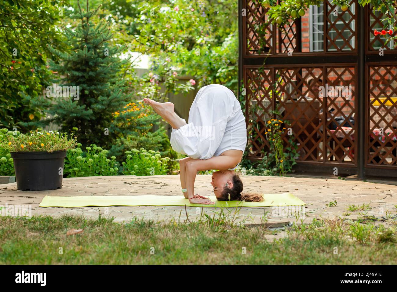 Young woman practices yoga in courtyard of a country house. Headstand - Ardha Salamba Shirshasana Stock Photo