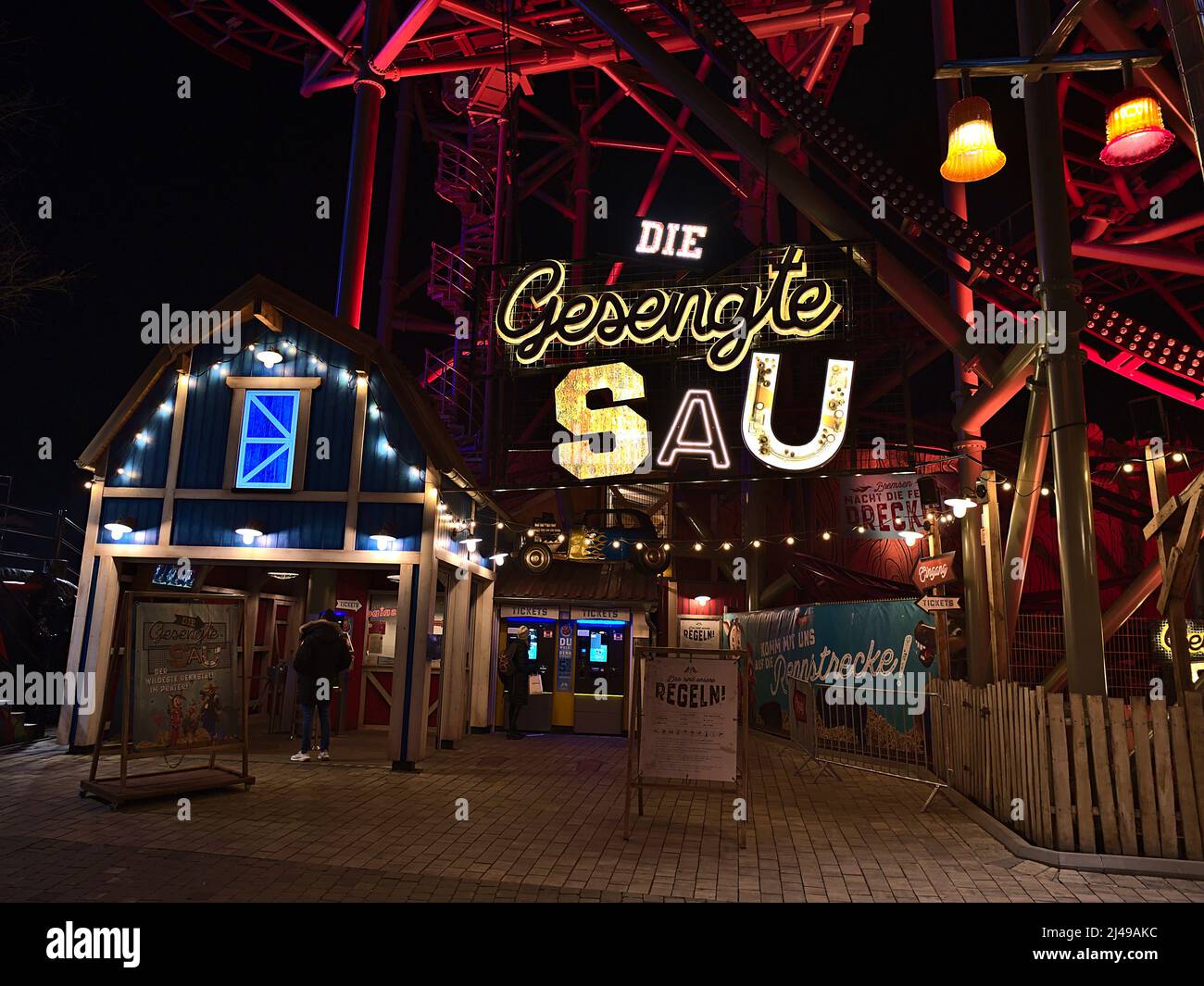 View of the entrance of roller coaster 'Die Gesenkte Sau' in popular park Wurstelprater in Vienna, Austria at night with people in front. Stock Photo