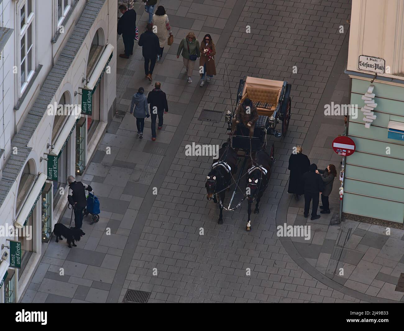 Aerial view of a fiacre, a horse-drawn four-wheeled carriage, with tourists passing people in a narrow street in the center of Vienna, Austria. Stock Photo