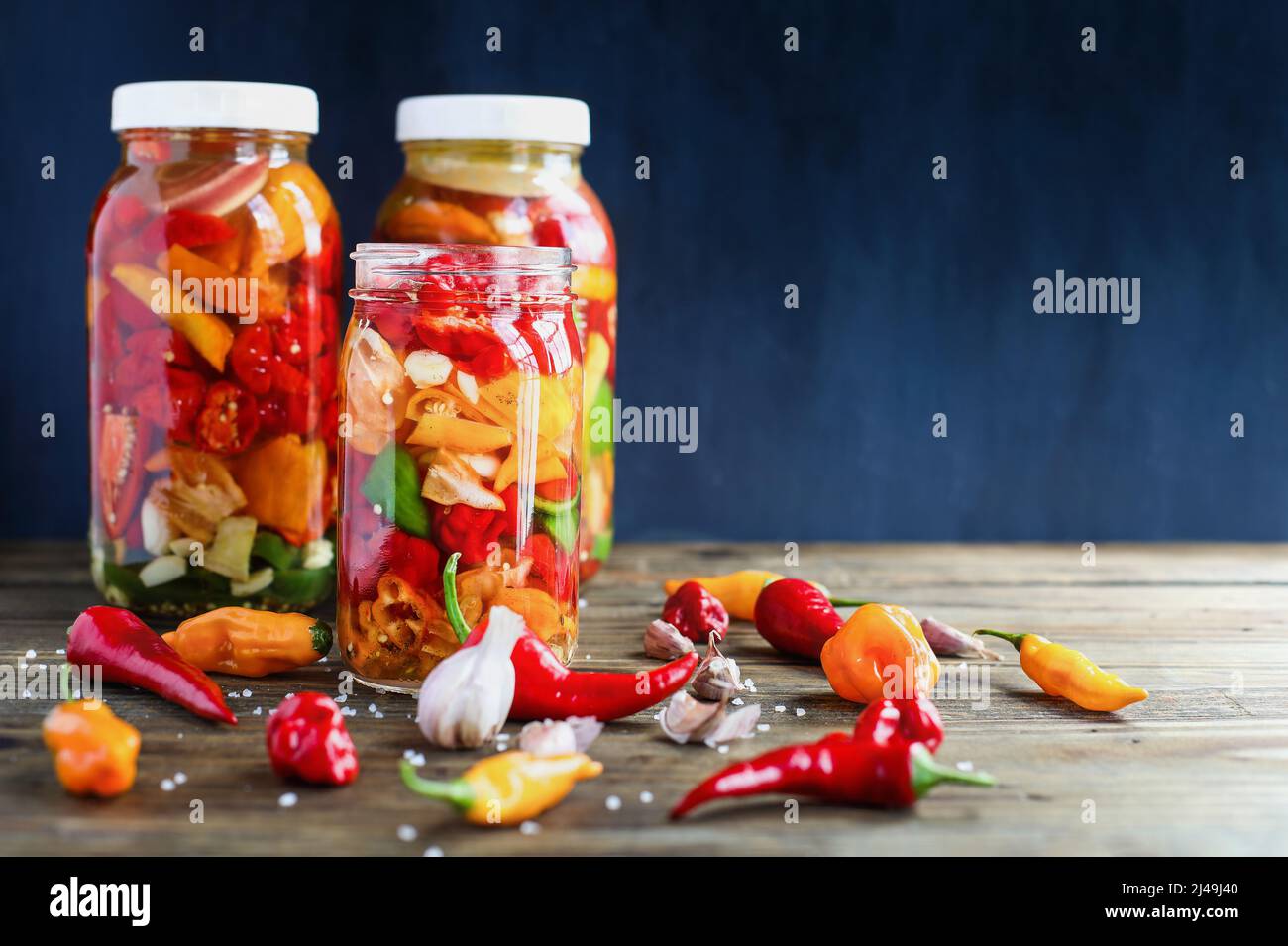 Variety of peppers, spices and garlic in a mason jars fermenting, a rich source of probiotics, to make homemade hot sauce over a rustic background. Stock Photo