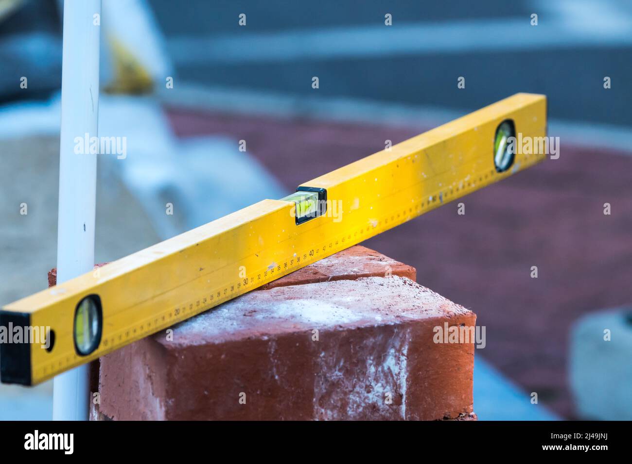 yellow spirit level on a pile or stack of red bricks concept building or construction work tool used for paving and repair of a pavement or sidewalk Stock Photo