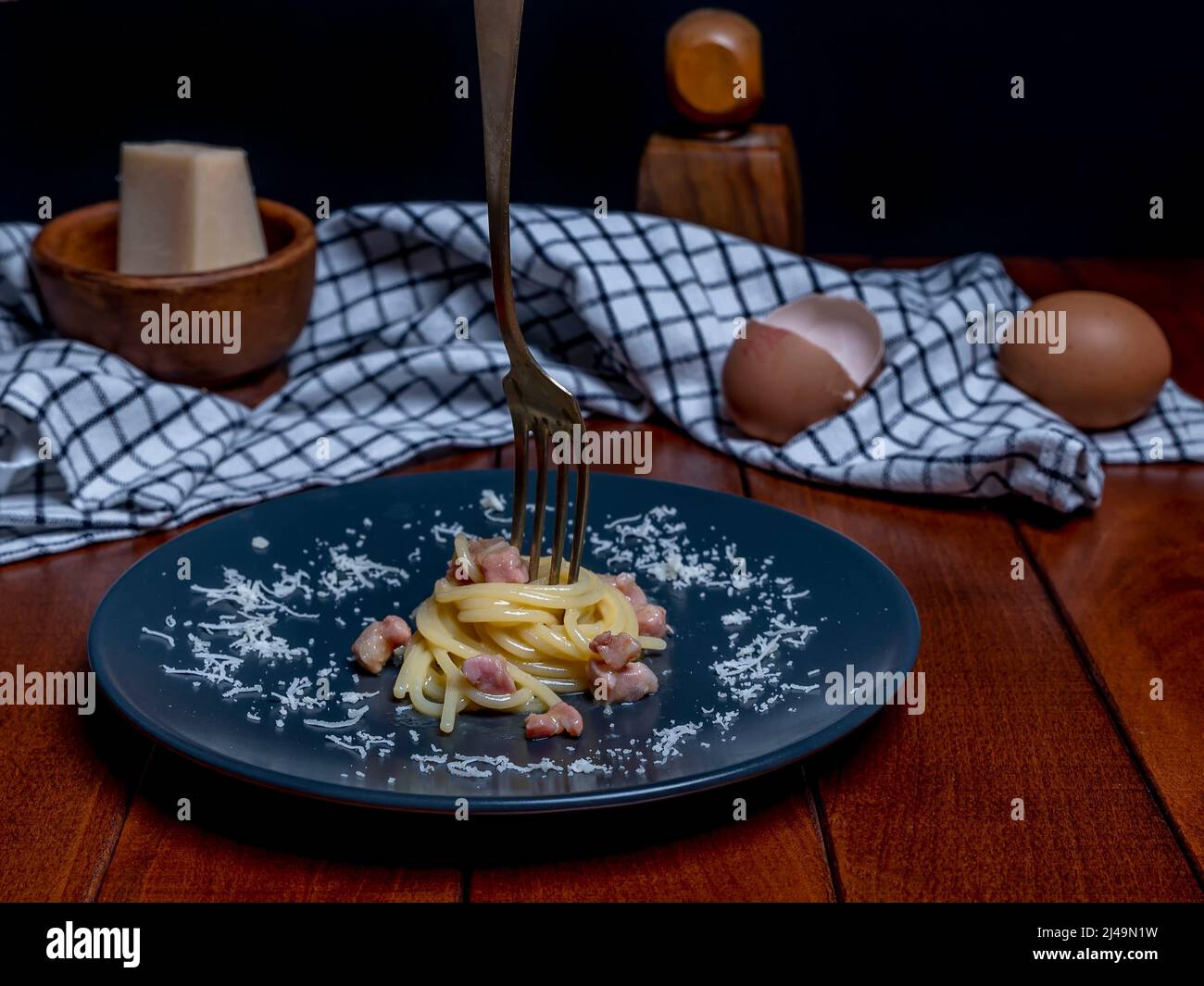A plate of carbonara-style rolled spaghetti, with a fork skewered on top Stock Photo