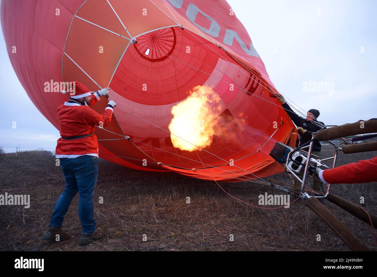 Men dressed as Santa Claus preparing hot-air balloon for launching, gas burner flaming. January 12, 2020. Kiev, Ukraine Stock Photo
