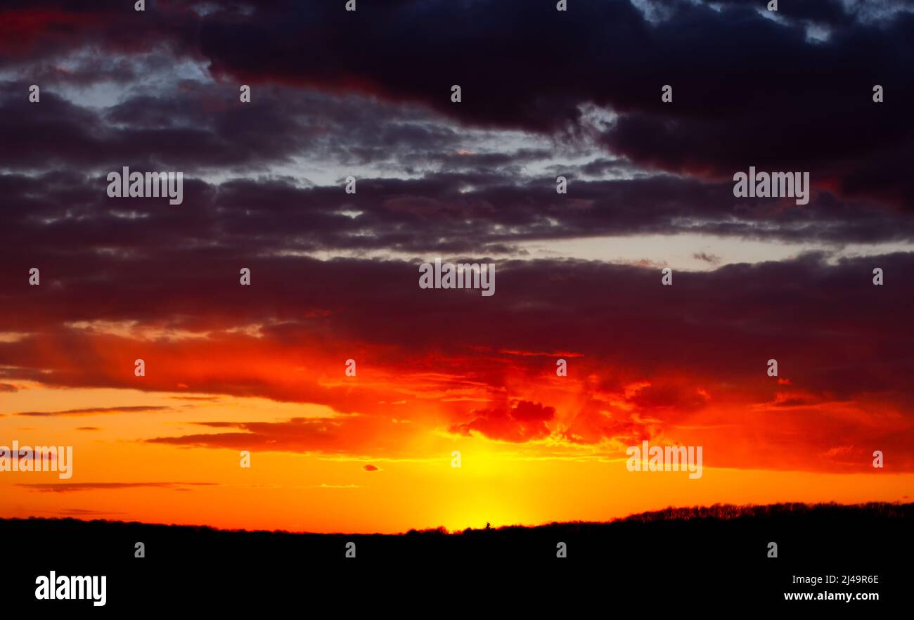 Abstract burning sky at sunset. Red clouds on the horizon are illuminated by evening sunlight. Stock Photo