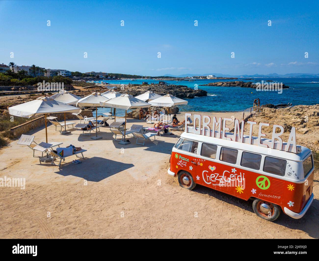 Classic Volkswagen red and white Type 2 camper van on Es Pujols beach, Chezz Gerdi bar beach restaurant advertising, Balearis Islands, Formentera, Spa Stock Photo
