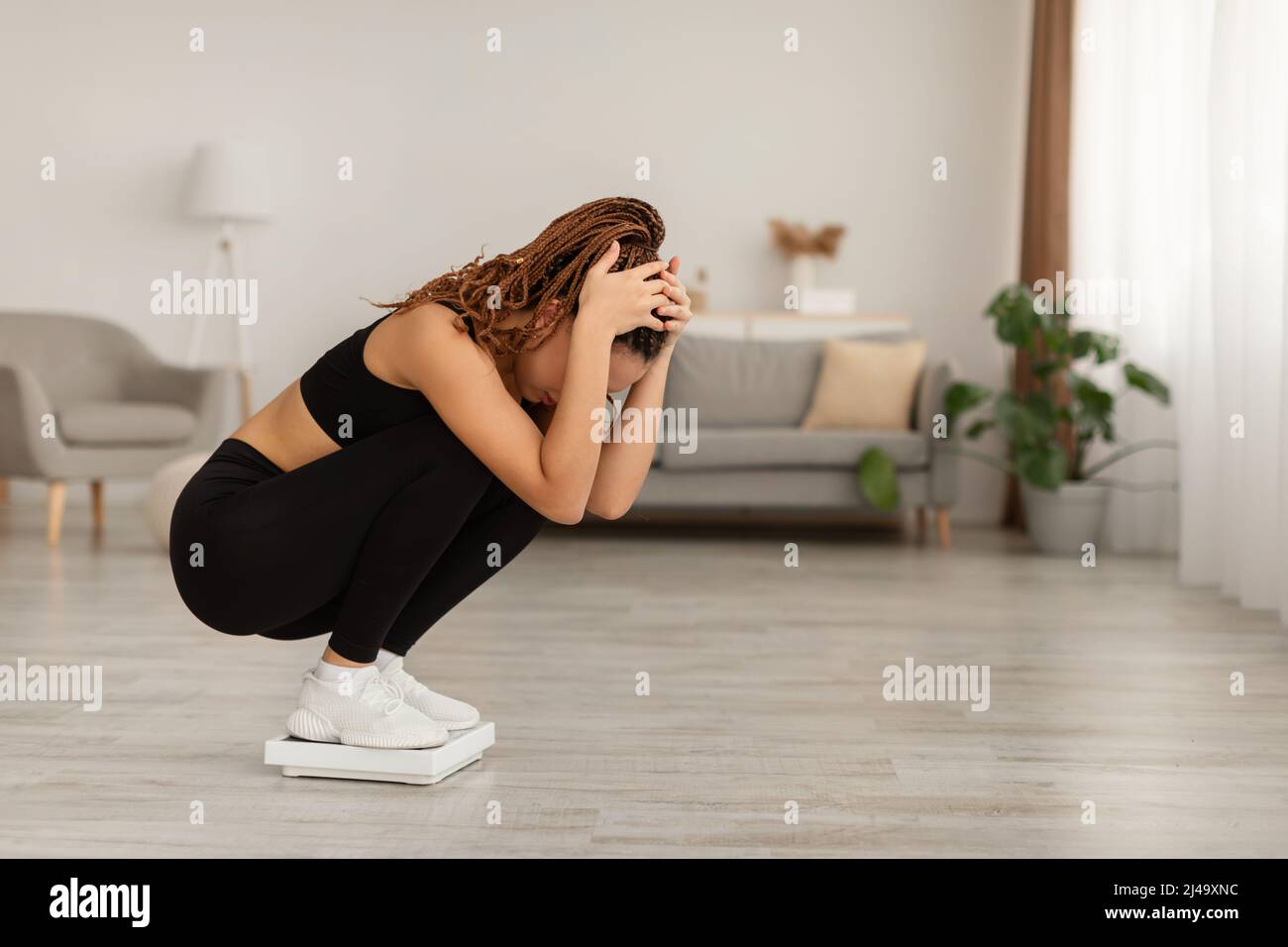 Unhappy Black Woman Weighing On Scales After Weight Gain Indoor Stock Photo