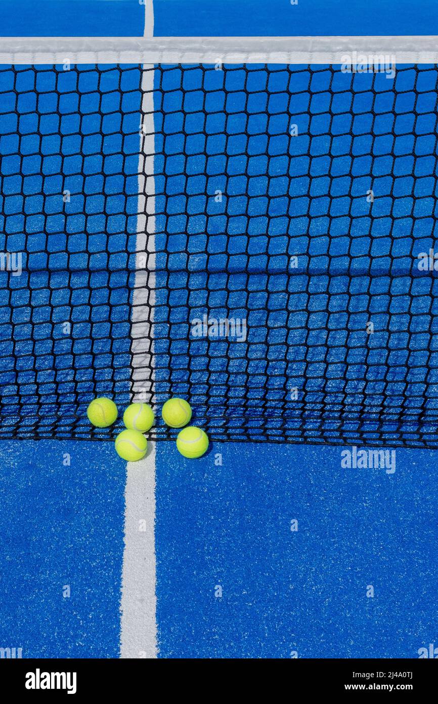 several paddle tennis balls by the net on a blue paddle tennis court