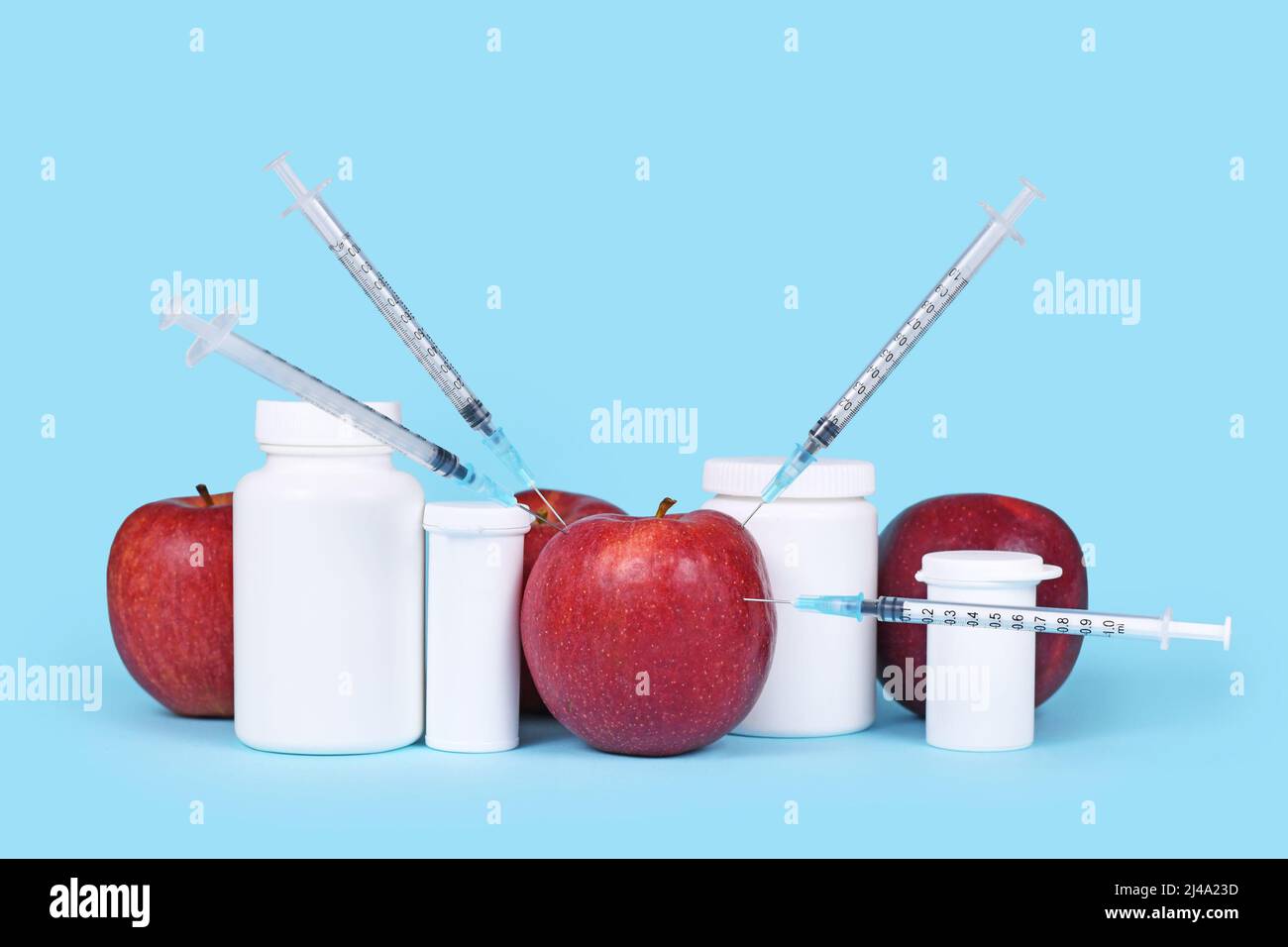 Apple fruits injected with syringes next to pill bottles. Concept for genetically modified food or pesticides Stock Photo