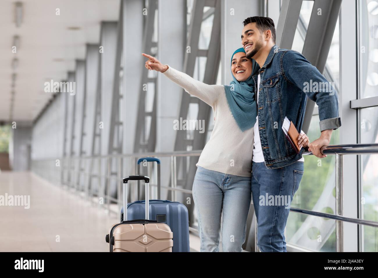 Joyful Muslim Couple Standing With Luggage At Airport And Pointing Away ...