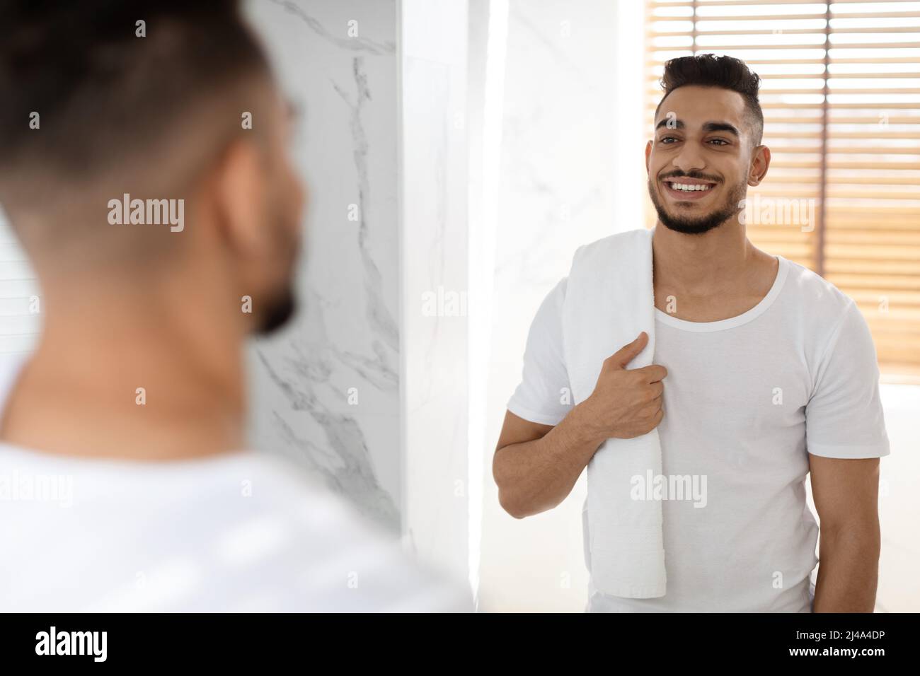 Happy Handsome Middle Eastern Man Holding Towel And Smiling To Mirror Stock Photo