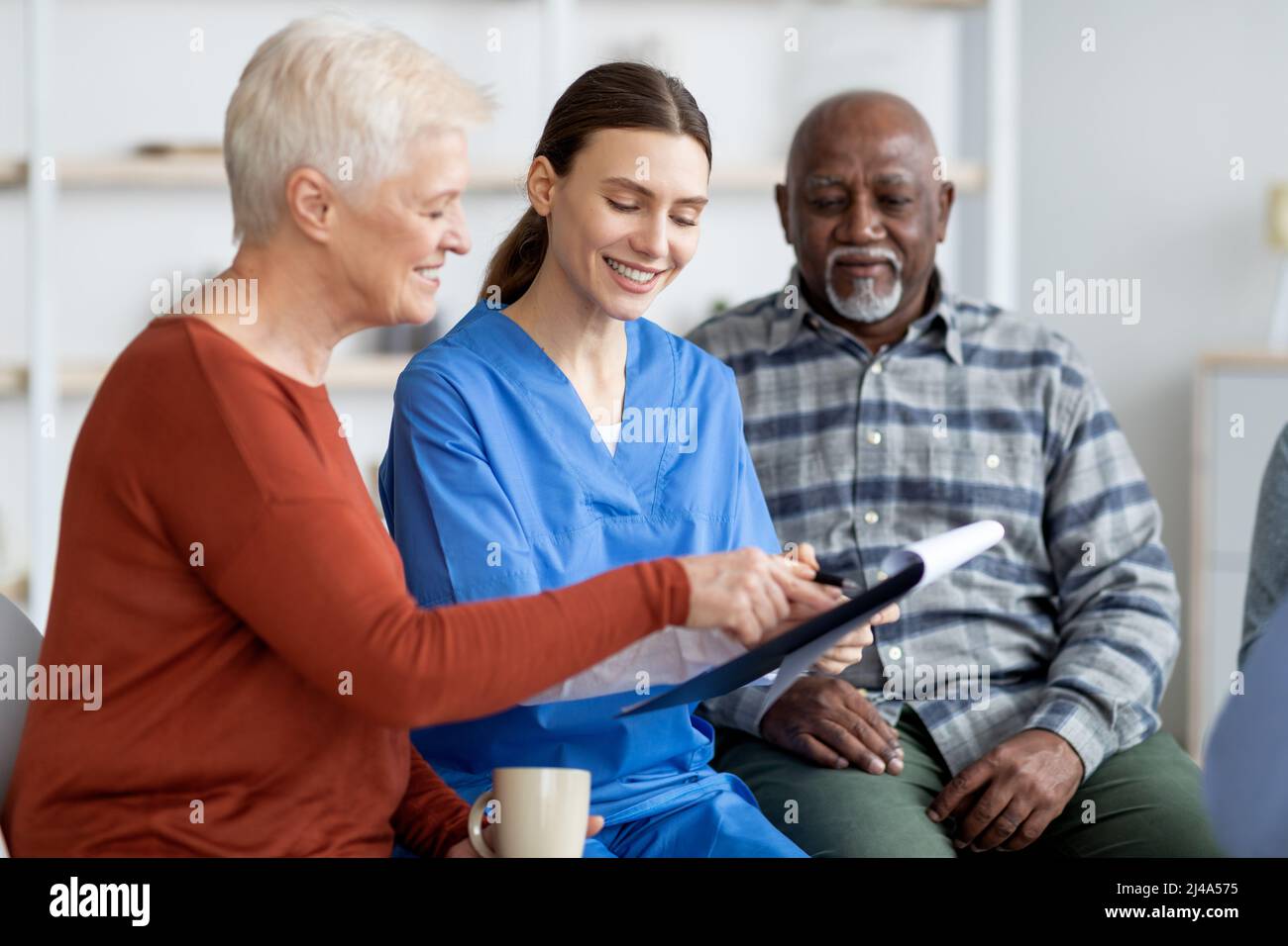Cheerful young woman doctor having conversation with senior patients ...