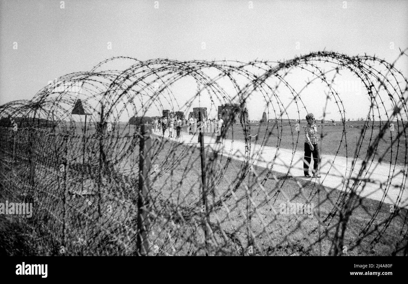 1976 archive photograph of visitors to Stonehenge behind barbed wire erected before pop festival. Stock Photo