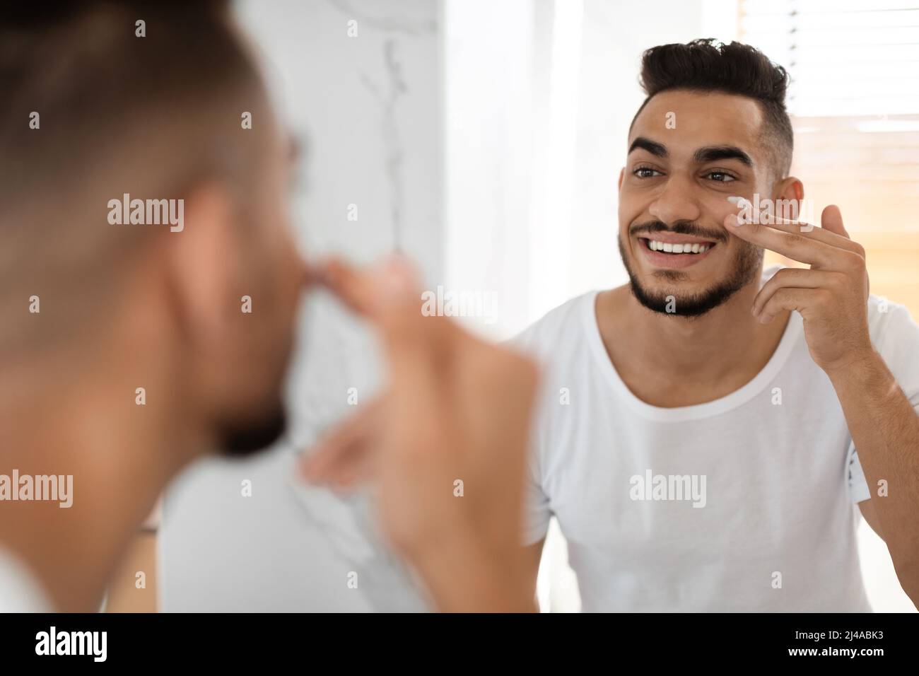 Skincare Routine. Attractive Middle Eastern Guy Applying Moisturising Cream On Face Stock Photo