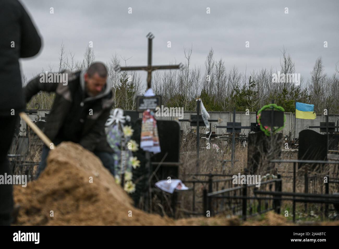 Bucha, Kyiv Oblast, Ukraine. 13th April, 2022. A Ukraine flag waves as a man covers the grave of Andriy Verbovyi, a territorial defense soldier, killed by Russians in Bucha, Kyiv Oblast, Ukraine on April 13, 2022 Credit: Piero Cruciatti/Alamy Live News Stock Photo