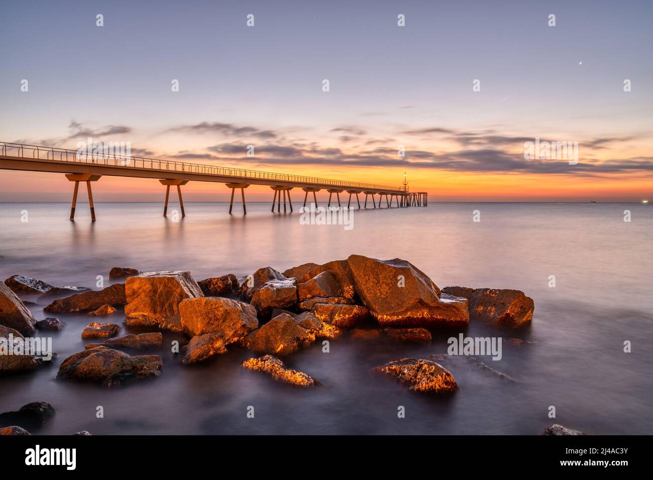 The sea pier of Badalona in Spain with some rocks before sunrise Stock Photo