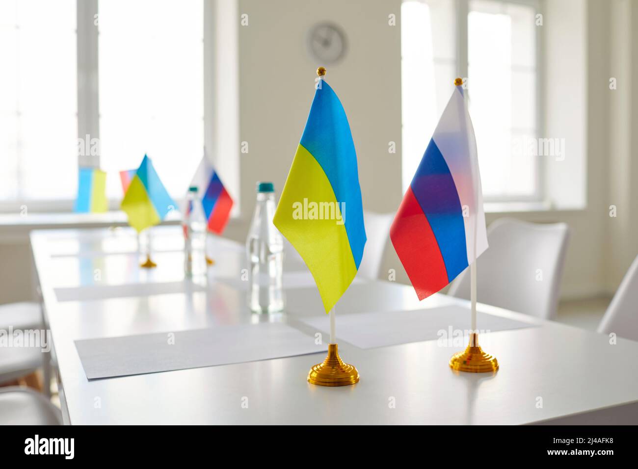 Table with flags of Russian Federation and Ukraine in empty room before negotiation meeting Stock Photo