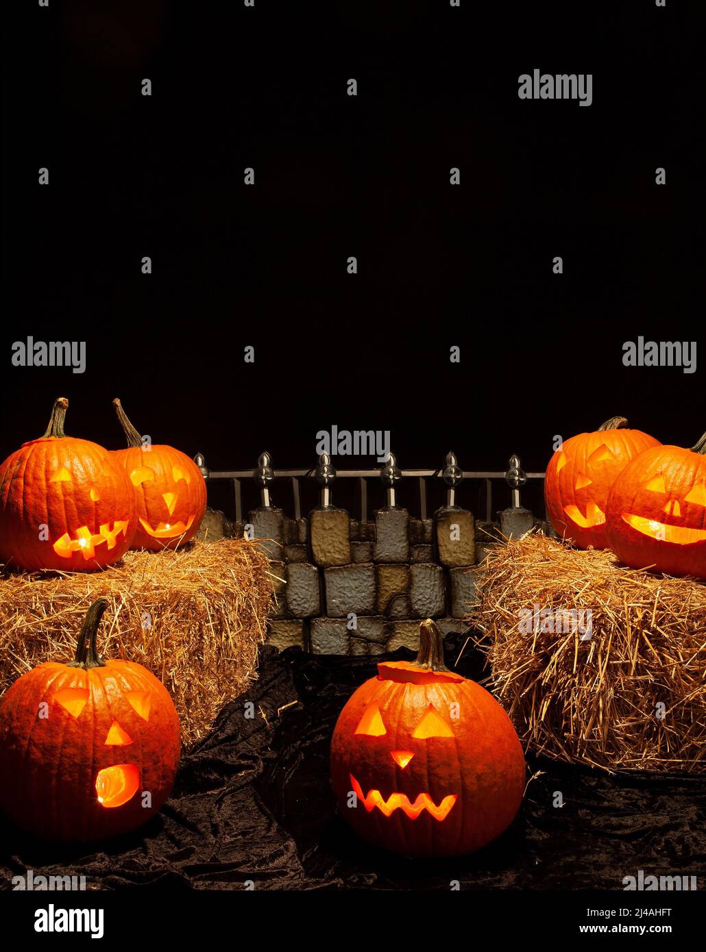 Spooky Halloween Scene with Jack-o-lanterns, hay and a spooky fence Stock Photo