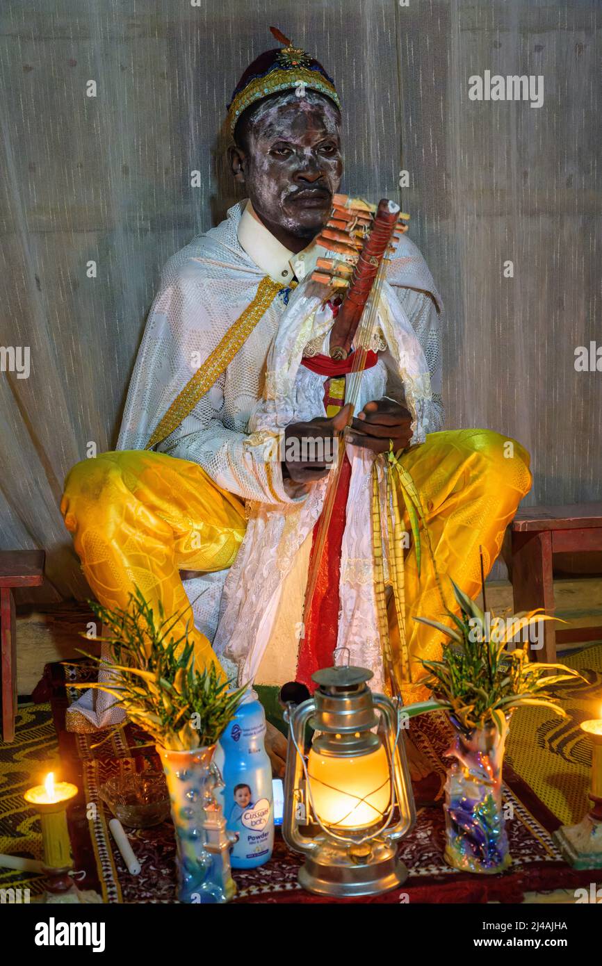Priest in white painted face playing the Ngombi, a traditional harp ...