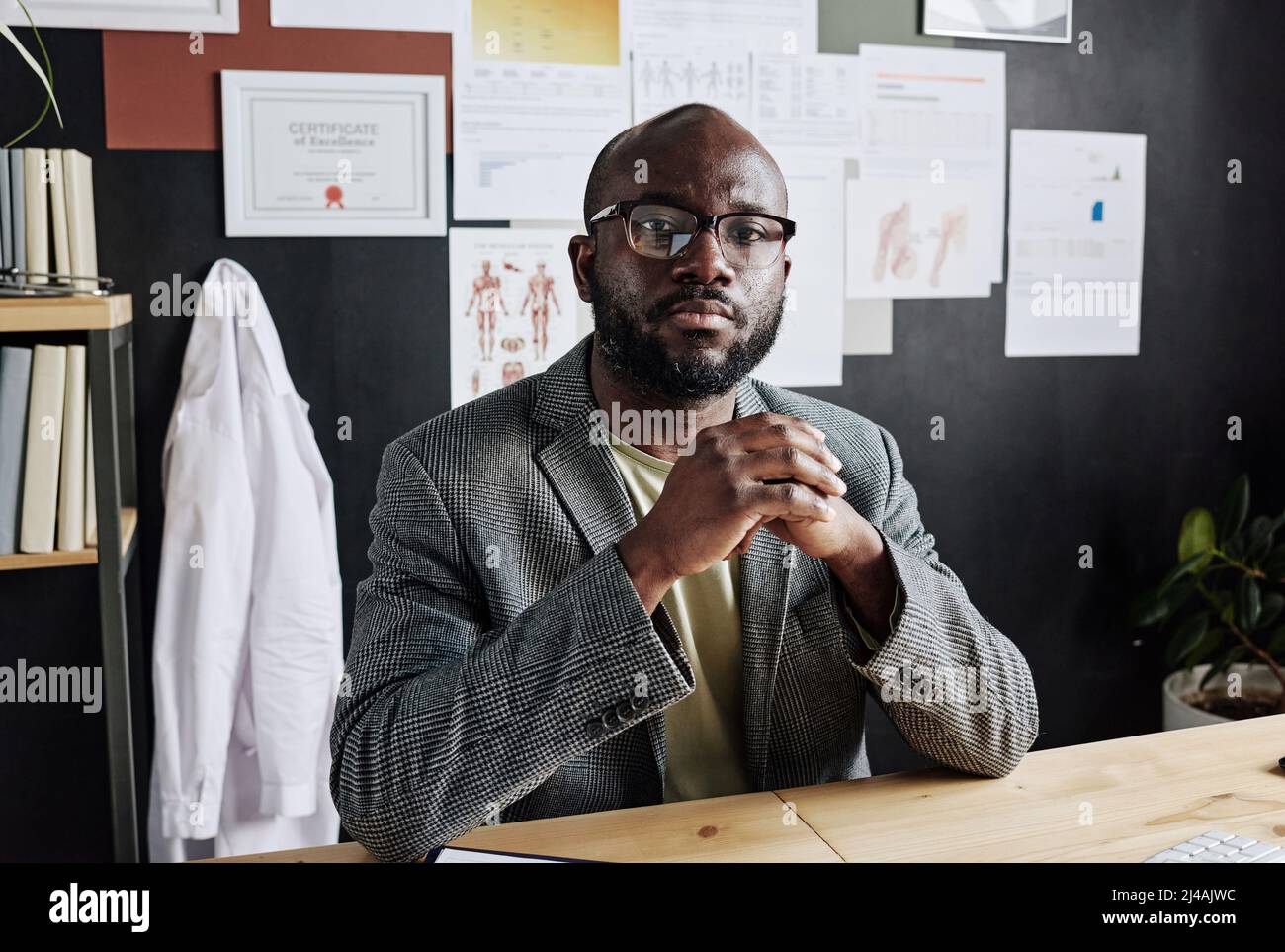 Portrait of African male doctor in eyeglasses looking at camera while sitting at table and working at office Stock Photo