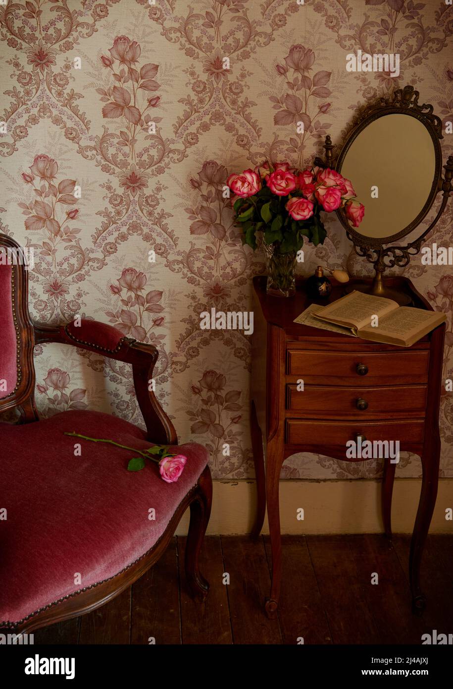 Vintage room with velvet armchair, antique mirror, pink roses and old book Stock Photo