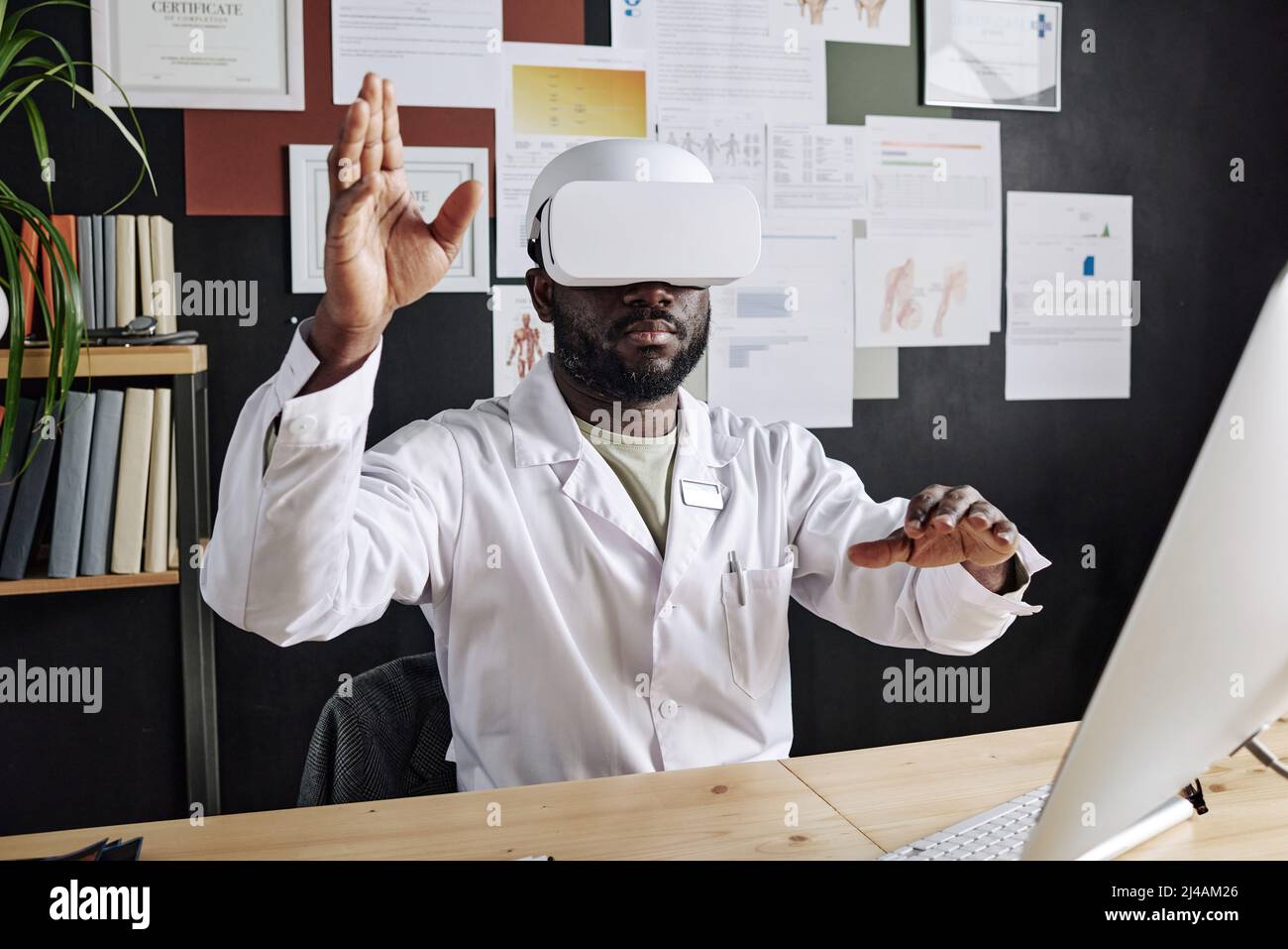 African doctor in virtual glasses gesturing in air while sitting at his workplace at office Stock Photo