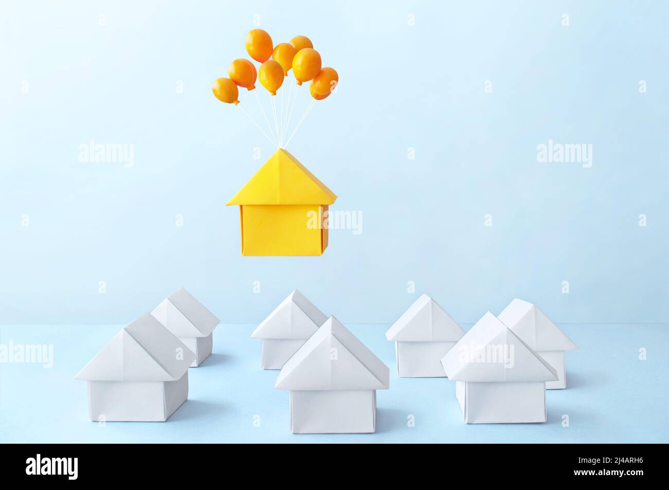 Orange paper house with balloons floating above many houses Stock Photo