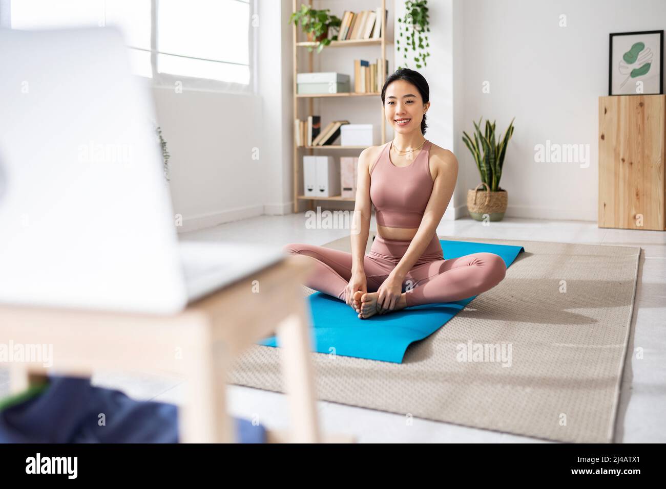 Premium Photo  Asian young woman practicing yoga on mat while sitting in  front of her laptop computer at home.
