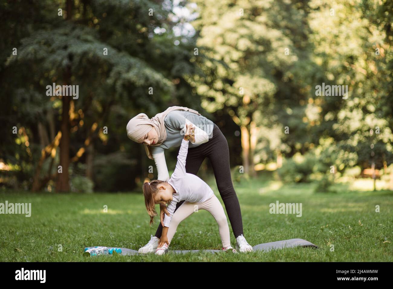 Outdoor fitness activity. Likable attractive Muslim woman in sportswear  teaching her preschool cute daughter how to do side tilts, enjoying leisure  time together in the summer park Stock Photo - Alamy