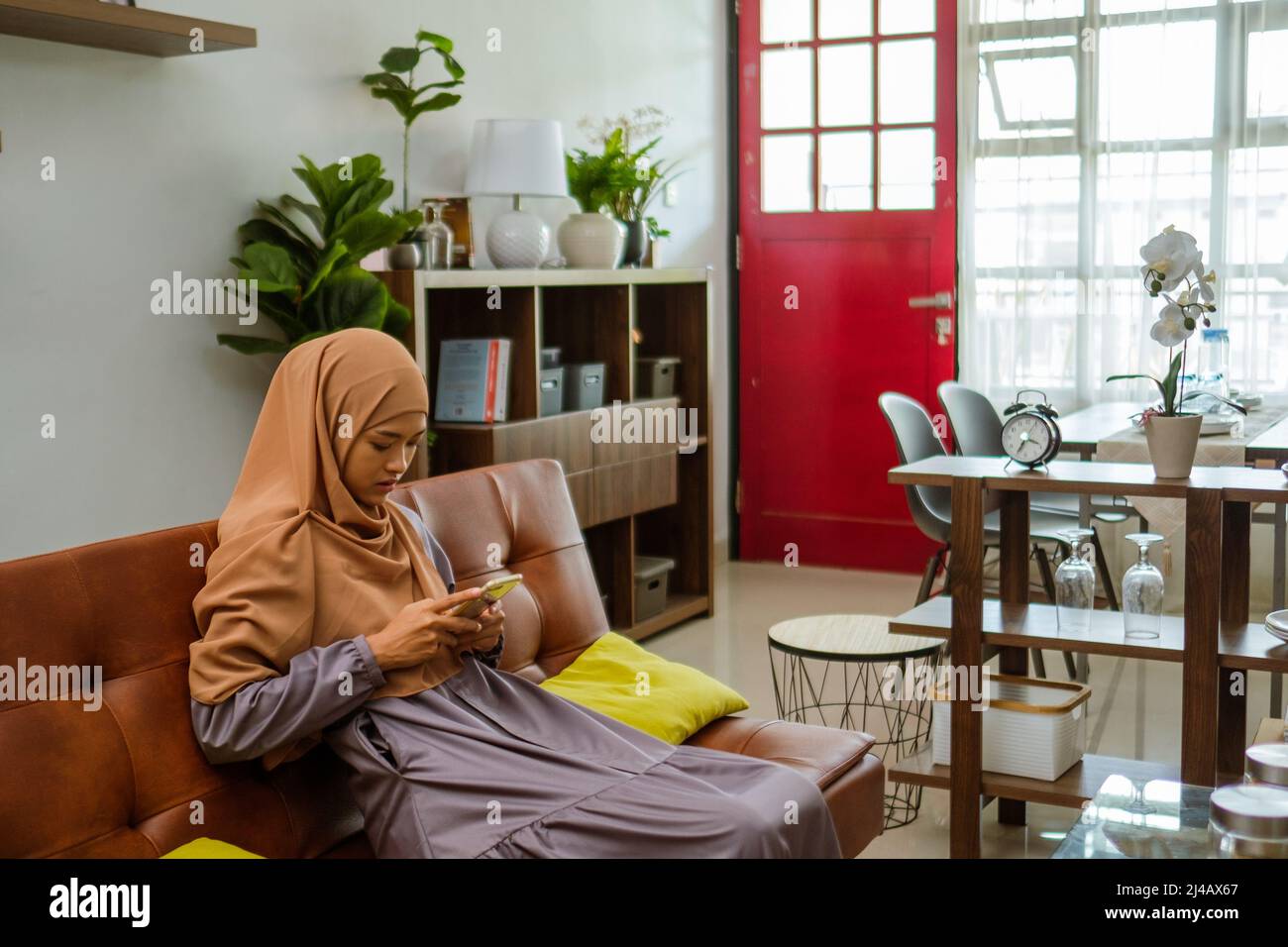 muslim woman sitting on sofa using her mobile phone Stock Photo - Alamy