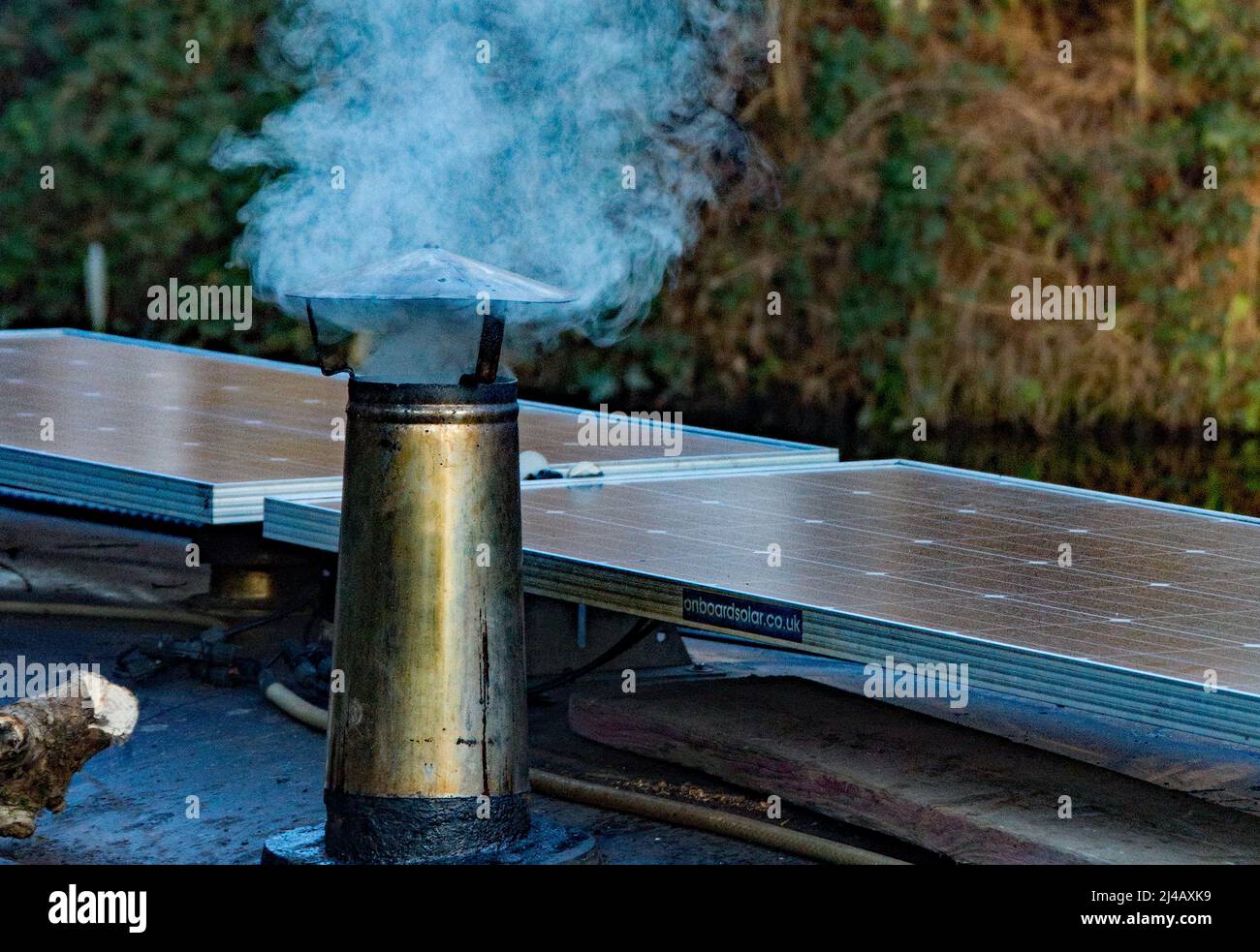 A smoke stack on a narrow boat keeping the crew warm on a winters day.  next to a modern solar panel the Lee and Stort canal at Sawbridgeworth. Stock Photo