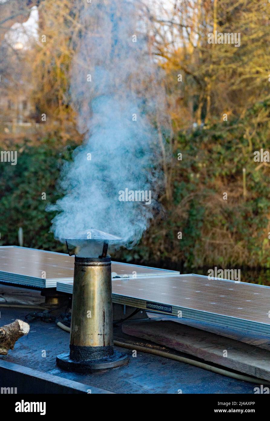 A smoke stack on a narrow boat keeping the crew warm on a winters day.  next to a modern solar panel the Lee and Stort canal at Sawbridgeworth. Stock Photo