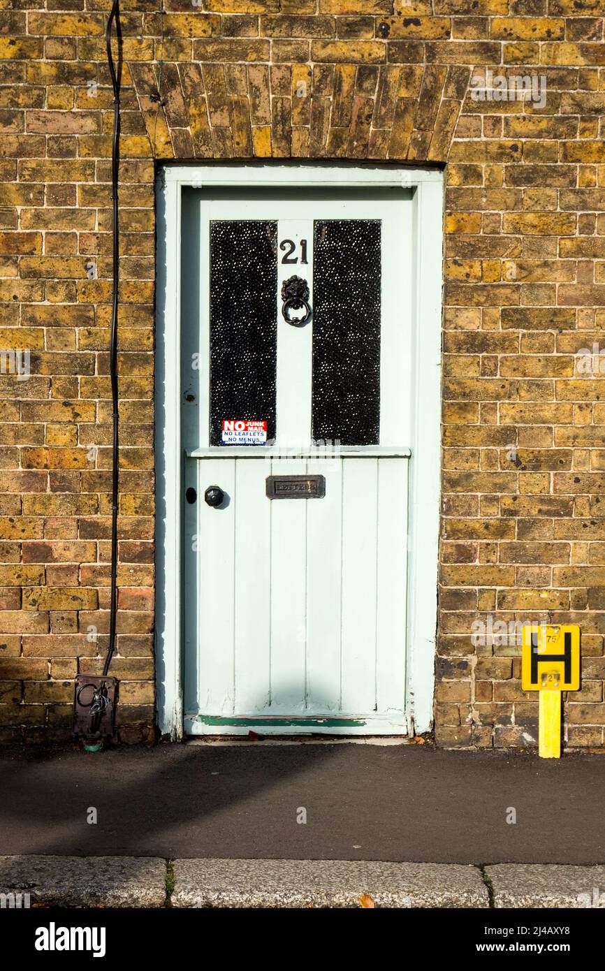 An old wooden village door with blacked door furniture and a number 21.  A sign demanding no junk mail.  Victorian era brickwork. Stock Photo