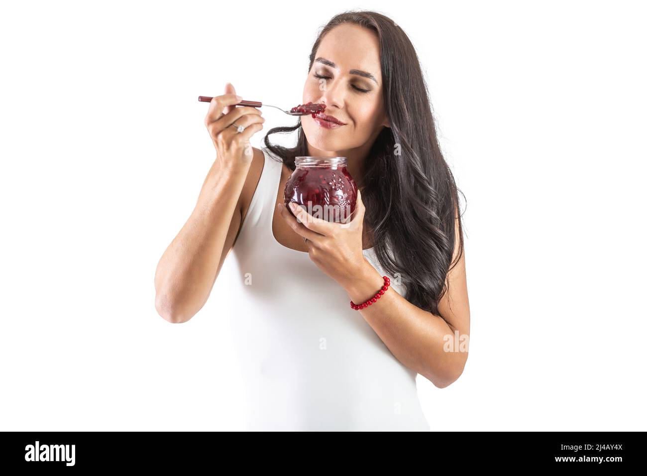 Charming brunette is holding a spoon sull of jam and smelling the tasty and sweet aroma. Isolated background. Stock Photo